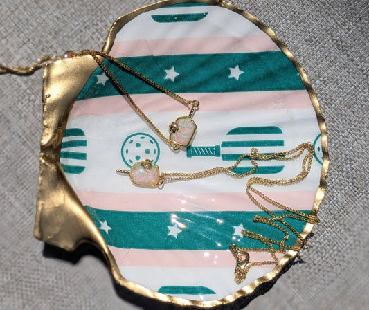 Gold chain necklaces with heart-shaped pendants displayed on a scalloped, patterned shell-shaped tray with a gray textured fabric background.